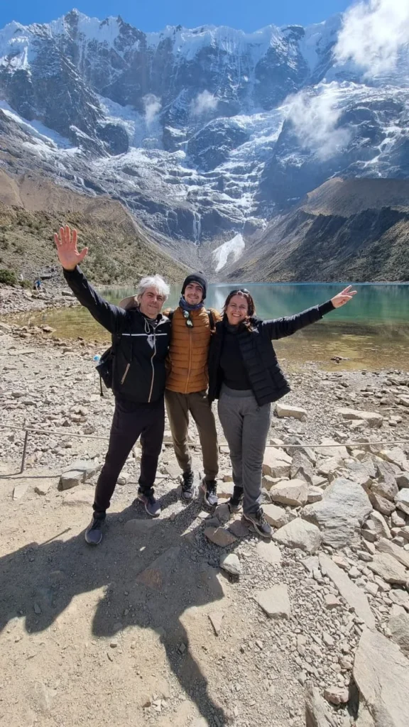 Três clientes da Monde Travel diante da Laguna Humantay, com montanhas nevadas ao fundo, na região de Cusco, Peru